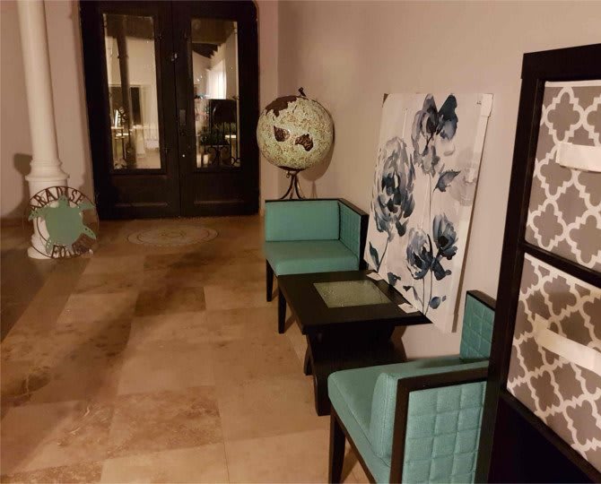 A stylish hallway featuring turquoise chairs, a globe, and floral artwork.
