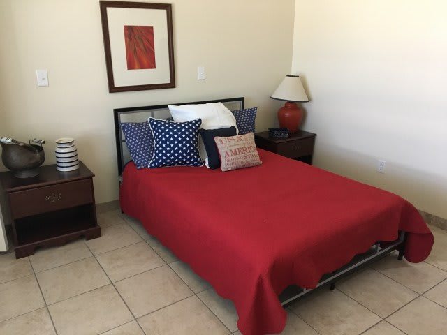 A neatly arranged bedroom with a red bedspread, decorative pillows, and a lamp on the nightstand.