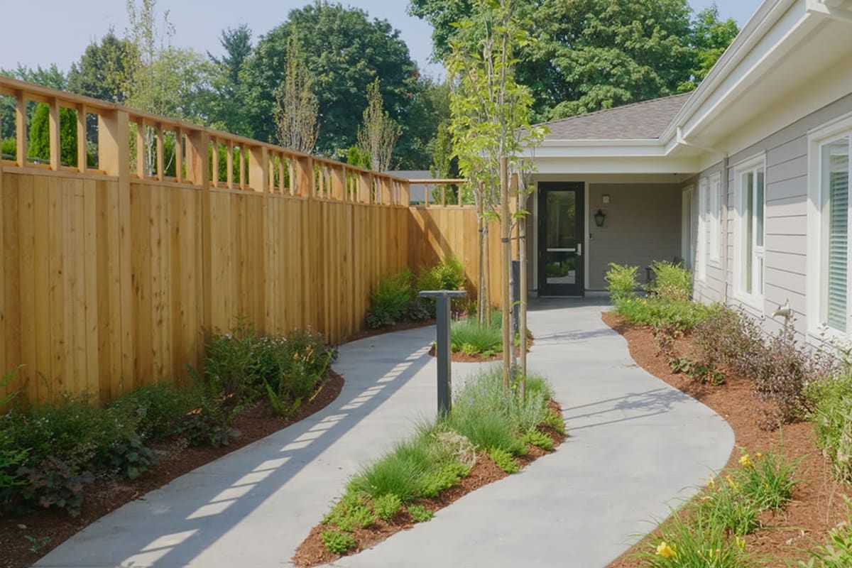 A landscaped garden pathway leads to a house entrance, bordered by a wooden fence and lush greenery.