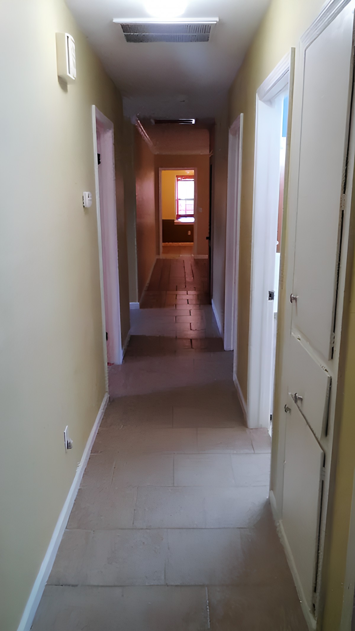 A hallway inside a home leading to a well-lit room in the distance.