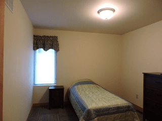 A minimalist bedroom with a single bed and a small nightstand beside a window.