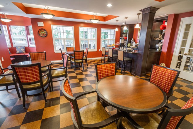 A cozy restaurant interior featuring round and square tables with checkered flooring and warm lighting.