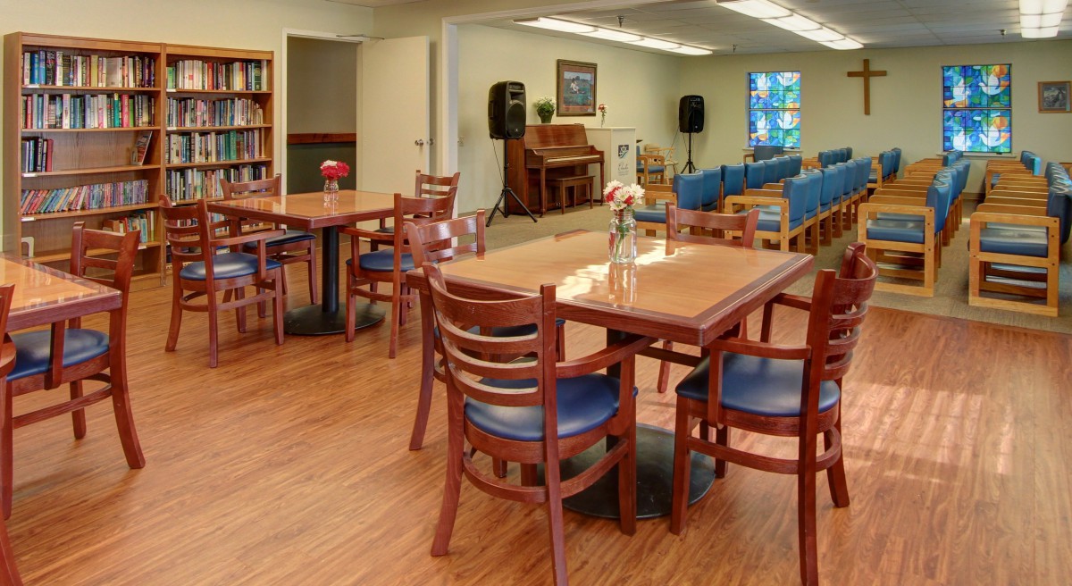 A cozy interior with tables and chairs, featuring a piano and bookshelf.