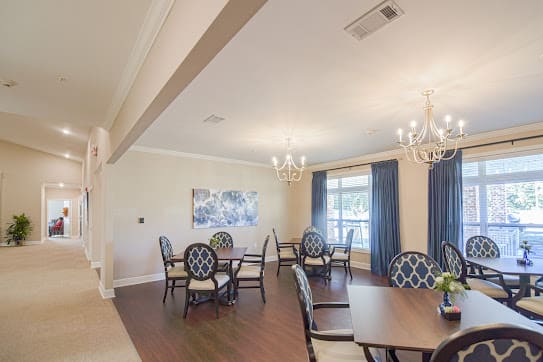 A well-lit dining room with elegant chandeliers, multiple tables and chairs, adorned with curtains and a wooden floor.