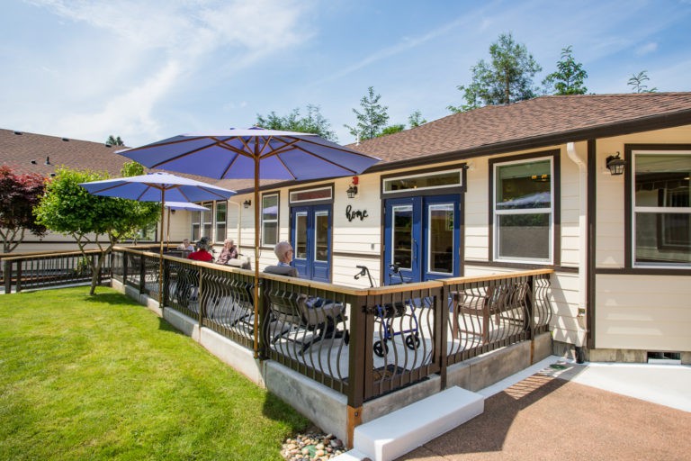 A cozy house with a spacious wooden deck featuring outdoor seating and large umbrellas on a sunny day.