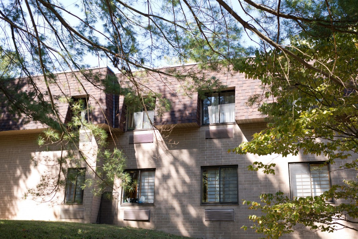 A residential building surrounded by trees, with sunlight casting shadows on its facade.