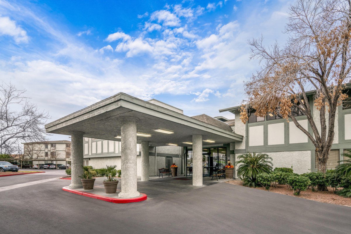 The entrance of a modern building with a covered driveway under a partly cloudy sky.