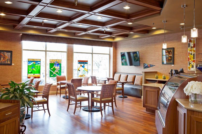 A modern cafe interior featuring wooden furniture, colorful artwork on the windows, and a cozy seating area.