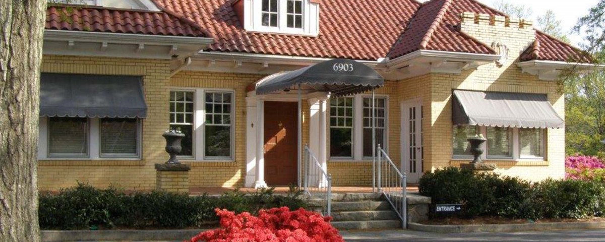 The entrance to a brick house with an awning, steps, and surrounding plants.