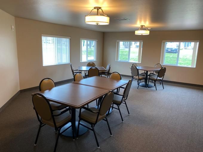 A spacious dining area with multiple tables and chairs, well-lit by overhead lighting and natural light from the windows.