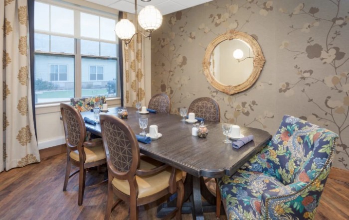 A well-decorated dining room with a large wooden table, elegant chairs, and a stylish mirror on the wallpapered wall.