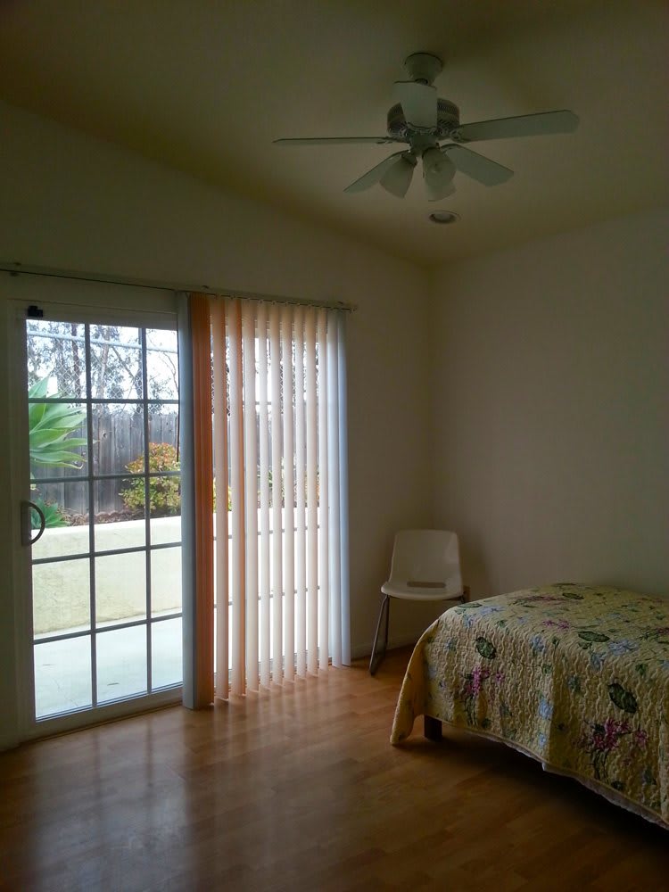 A cozy bedroom featuring a bed, chair, and sliding glass door with curtains.