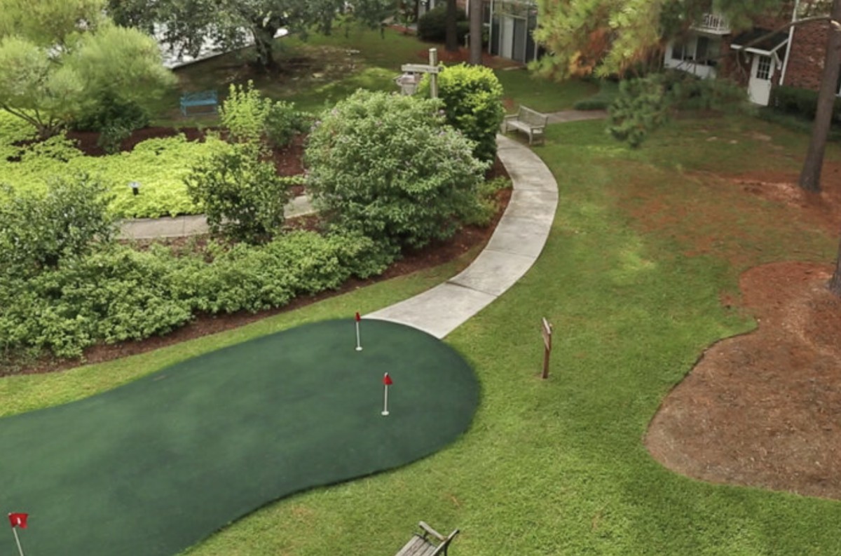 A well-maintained mini-golf putting green with a curved pathway set amidst lush landscaping.