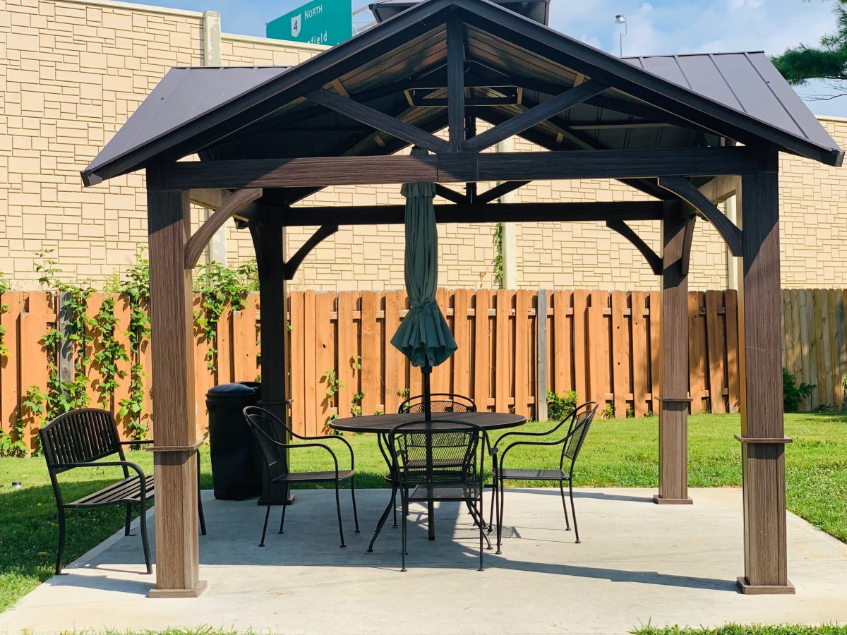 A cozy outdoor gazebo with a table and chairs set under an umbrella, surrounded by a wooden fence.