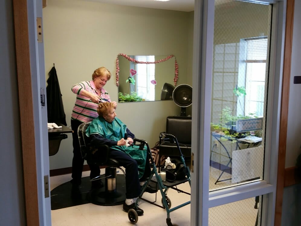 An elderly person in a wheelchair is getting a haircut from a hairstylist inside a hair salon.