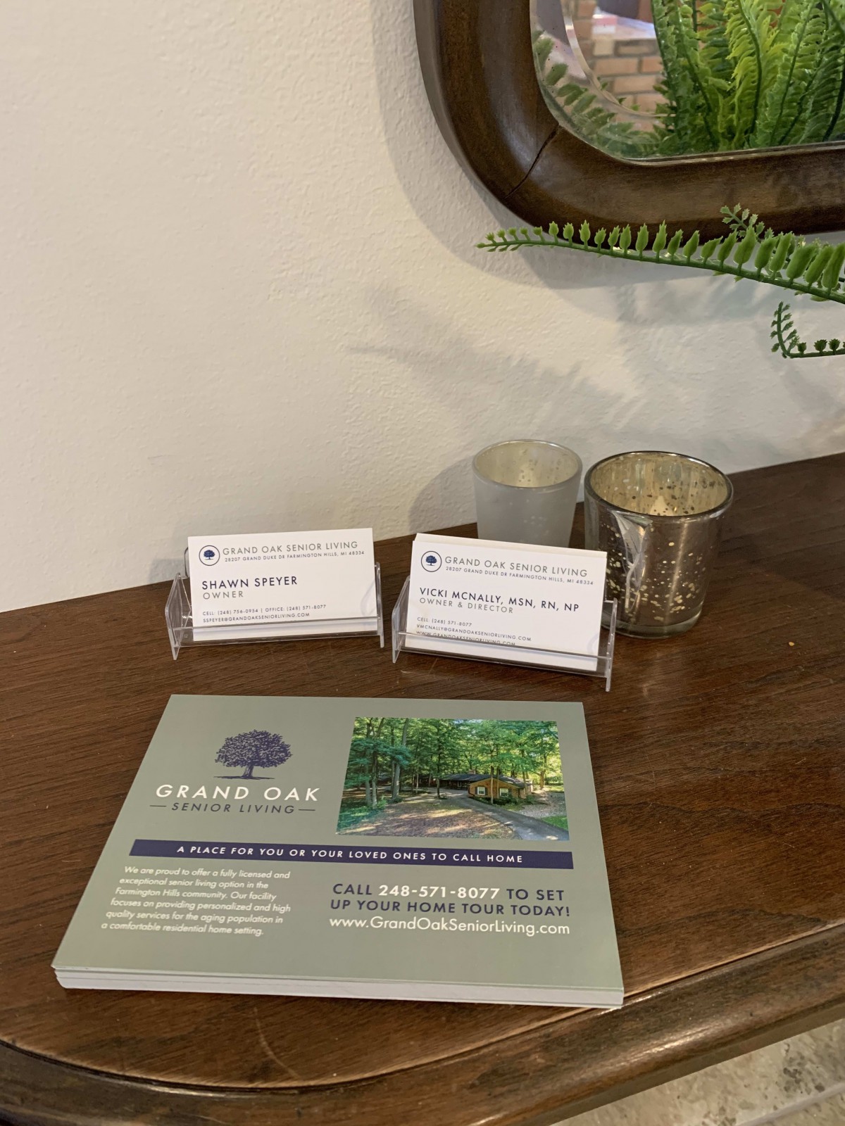 A set of business cards and candles displayed on a wooden table alongside a brochure, creating a professional and welcoming atmosphere.