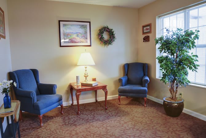 A cozy living room with two blue chairs, a wooden table, and a lamp.
