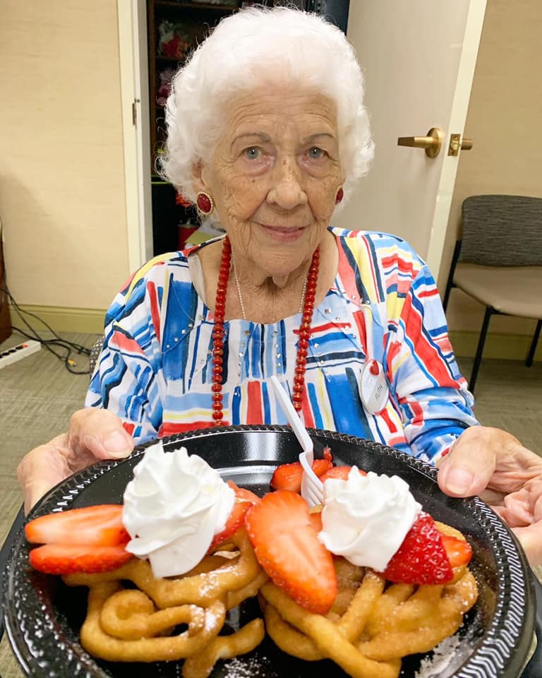 An elderly woman happily holding a plate of waffles topped with strawberries and whipped cream.