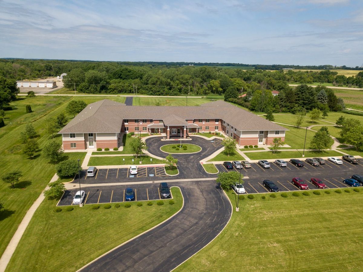 Aerial view of a large brick building with a surrounding parking lot and greenery.