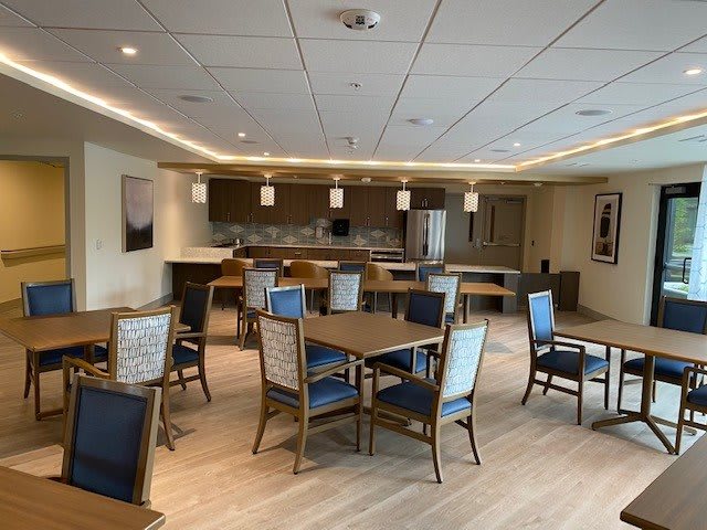 A modern dining area with a kitchen in the background, featuring tables and chairs.