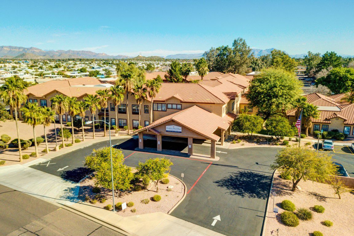 Aerial view of a building surrounded by palm trees and a parking lot on a sunny day.