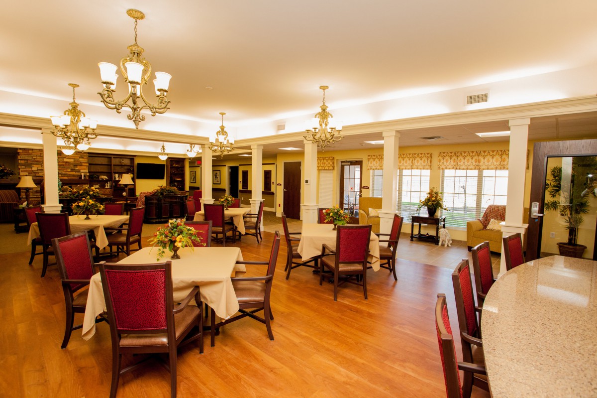 A well-lit dining room with neatly arranged tables and chairs, featuring elegant chandeliers.