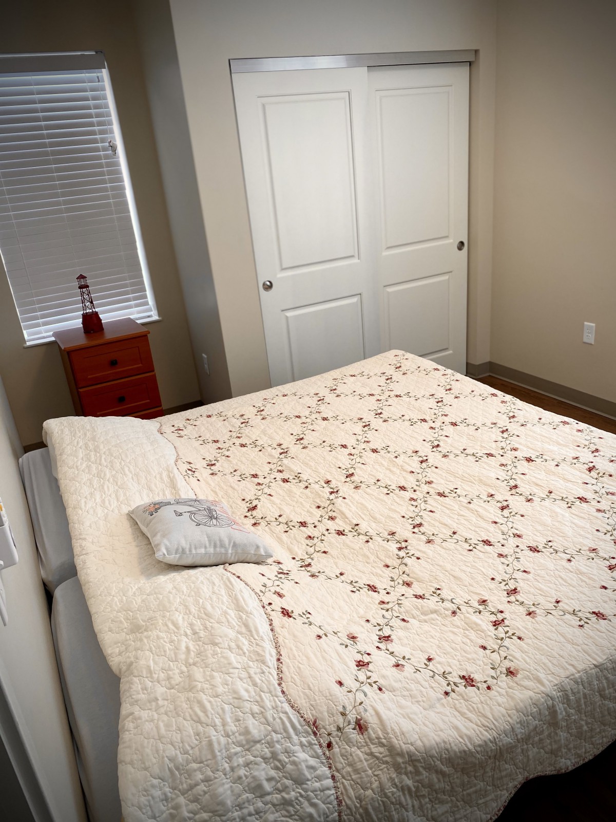 A cozy bedroom with a quilted bed, nightstand, and closed closet.