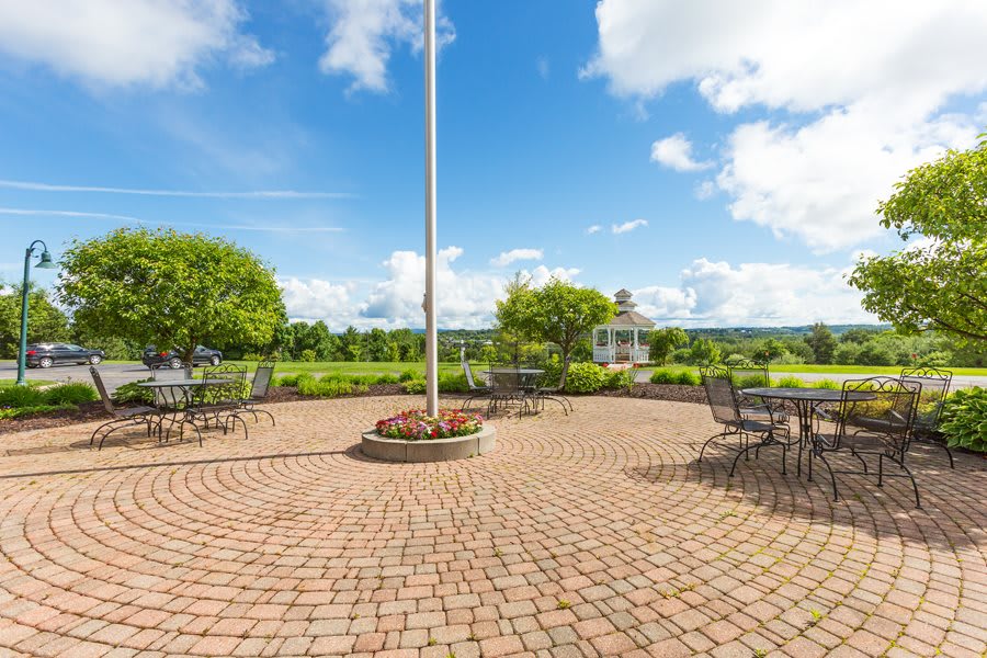 A scenic outdoor patio area with tables and chairs, surrounded by greenery and a cloudy sky.