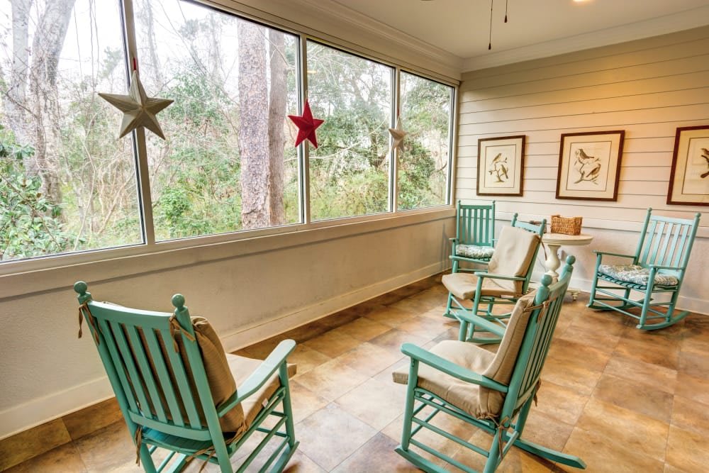 A cozy porch with teal rocking chairs and star decorations, offering a serene nature view through large windows.