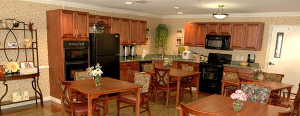 A cozy kitchen and dining area with wooden cabinets, a black refrigerator, and several dining tables.