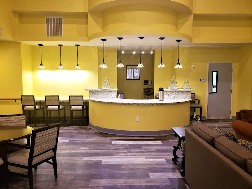 A modern reception area featuring bright yellow walls, stylish bar stools, and warm lighting.