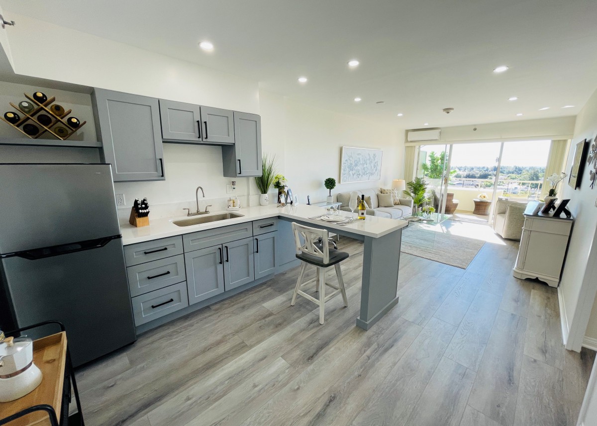 A modern open-concept kitchen with gray cabinets and wood flooring, featuring a central island and bright lighting.