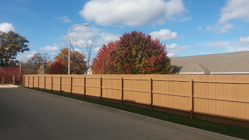 A serene autumn scene showcasing a wooden fence with vibrant trees and a clear blue sky.