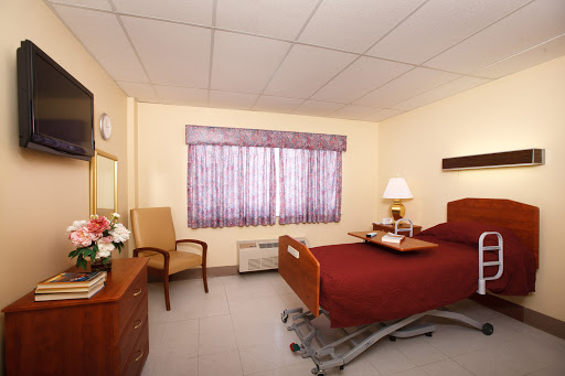 A comfortable hospital patient room featuring a bed, chair, and window with natural light.