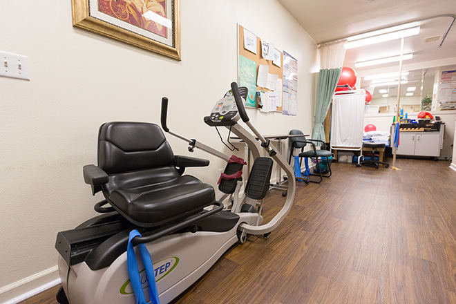 A healthcare facility room with exercise equipment, including a recumbent bike used for physical therapy.