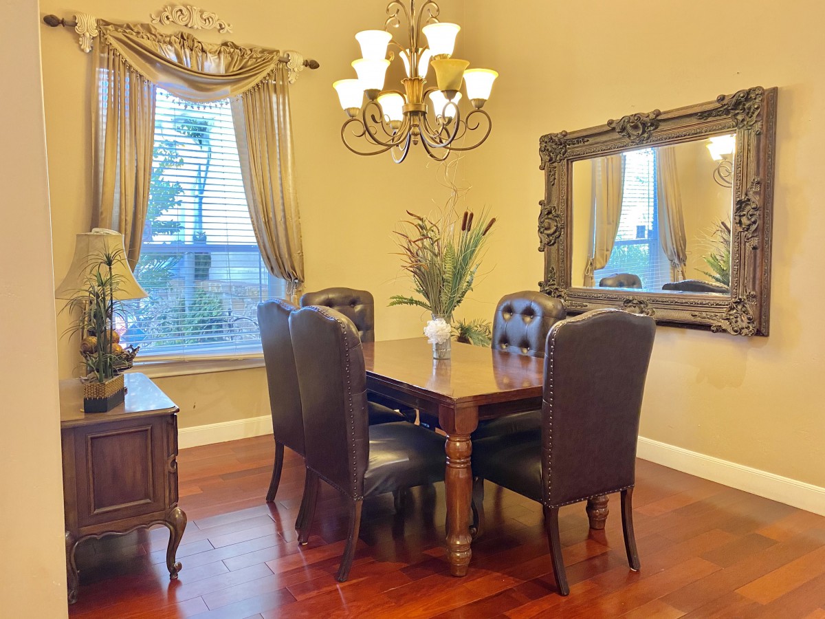 Elegant dining room with a chandelier, large mirror, and a wooden table surrounded by leather chairs.