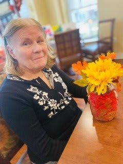 A woman sitting at a table with a vase of vibrant flowers.