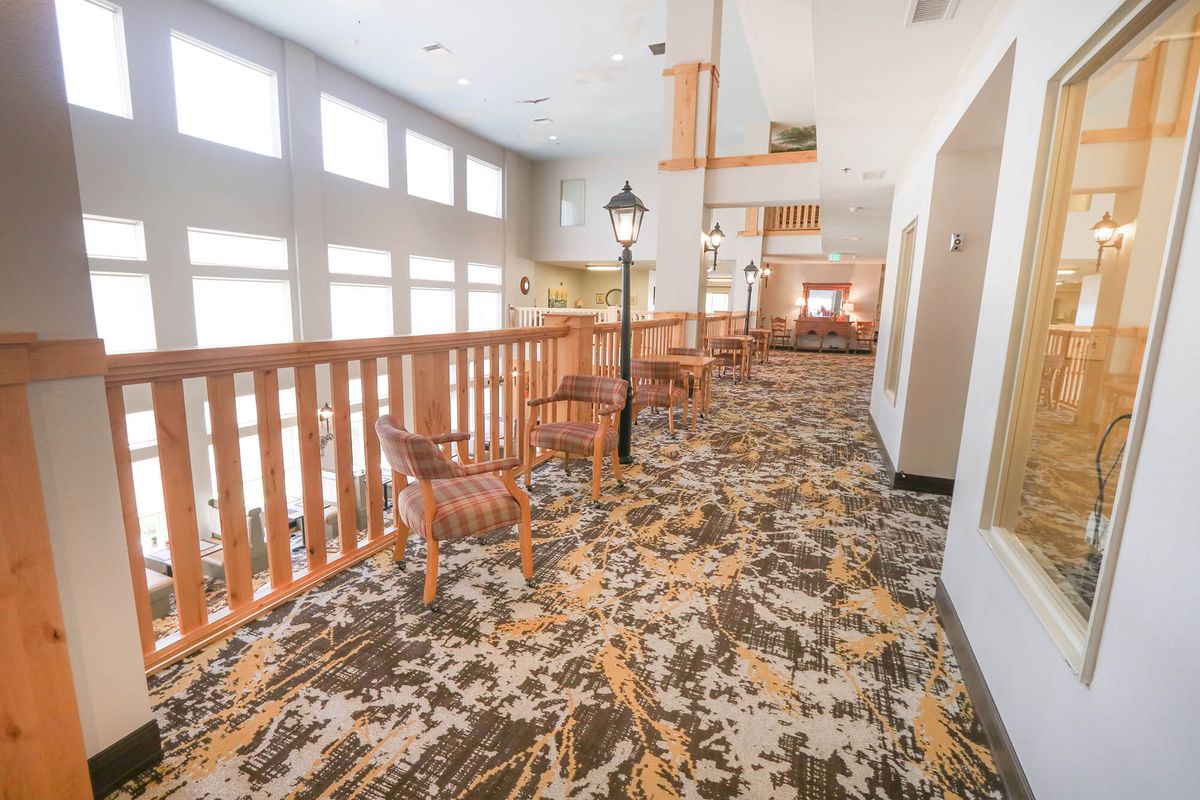 A bright corridor with wooden railings, patterned carpet, and seating areas along the side.