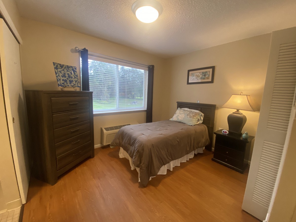 A cozy bedroom with a single bed, dresser, and a lamp by the window.