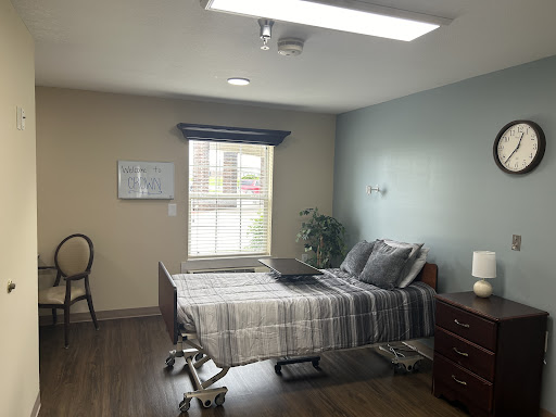 A well-lit hospital room featuring a bed, chair, and minimalistic decor.