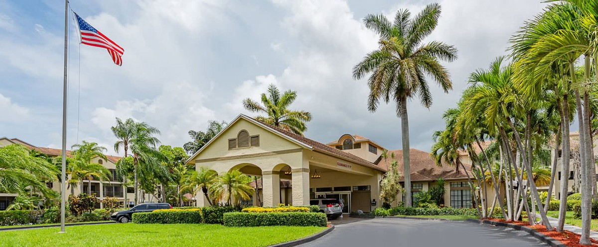 A beautiful house with a covered entrance surrounded by lush landscaping and palm trees under a cloudy sky.