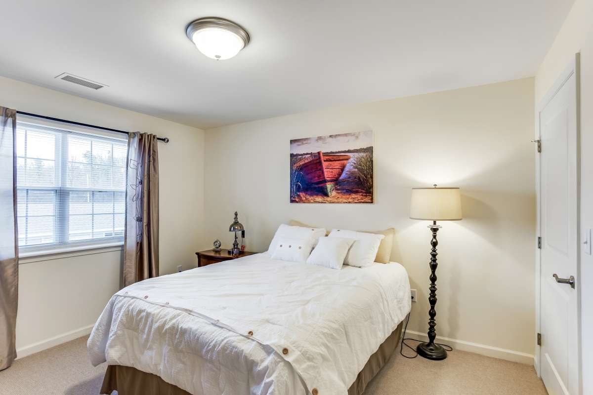A cozy bedroom with a neatly made bed, artwork on the wall, and warm lighting from a floor lamp.
