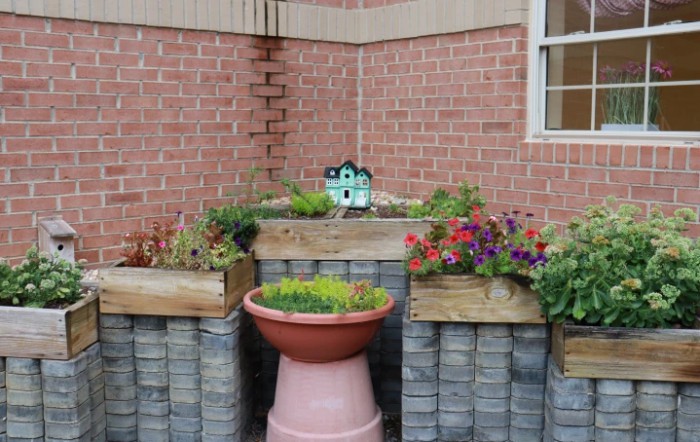 A variety of plants and flowers growing in raised garden beds against a brick wall.