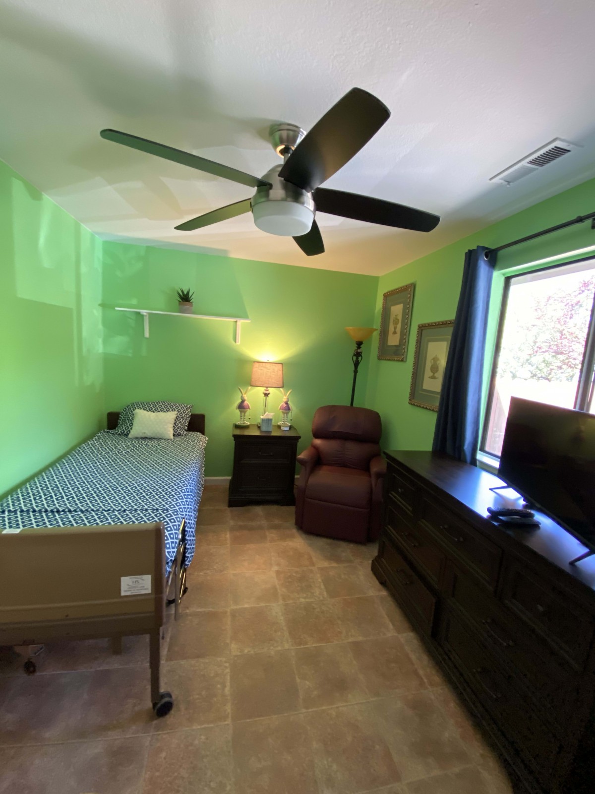 A compact bedroom with bright green walls featuring a single bed, recliner, dresser, and television.