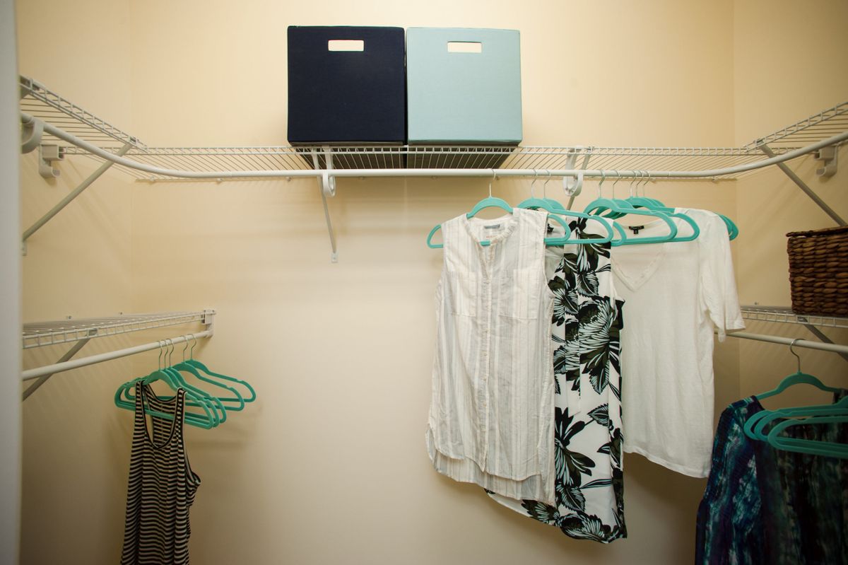 A well-organized closet with clothes hanging on teal hangers and storage boxes on the shelf.