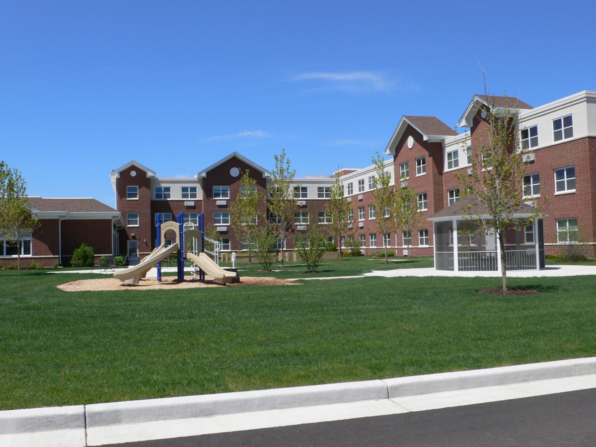 A residential building with a playground and green lawn on a sunny day.