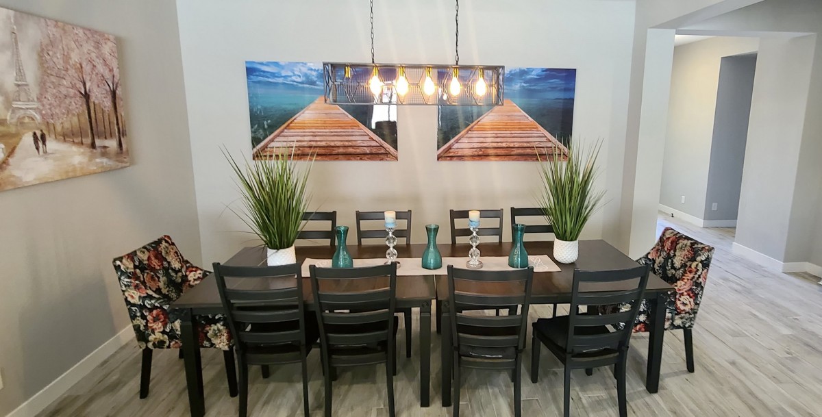 A dining room setup featuring a large table with chairs, plants as centerpieces, and scenic wall art.