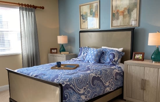 A cozy bedroom with blue patterned bedding, artwork on the walls, and a bedside lamp.