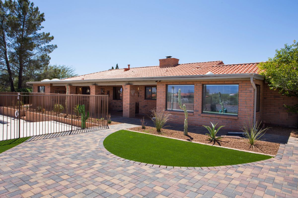 A single-story brick house with a tiled roof, featuring a landscaped front yard and paved driveway.
