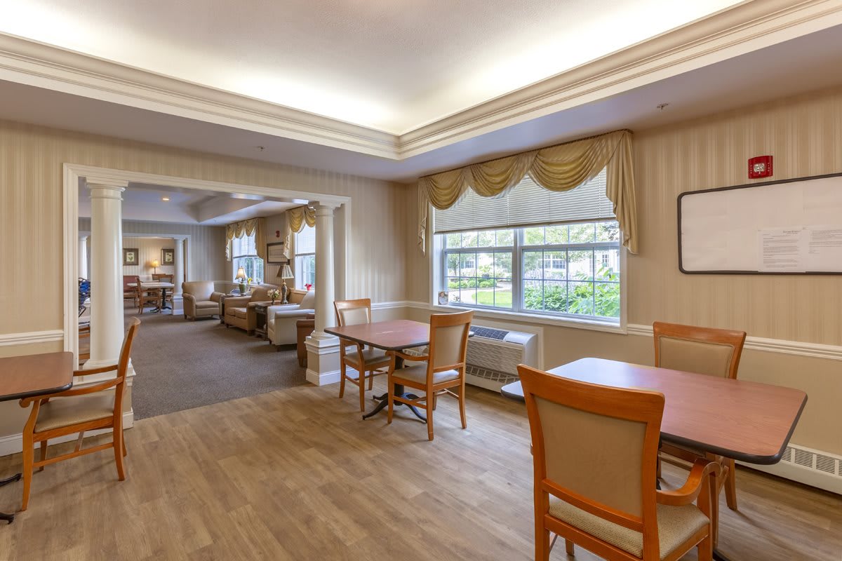 A cozy dining area with wooden tables and chairs, featuring large windows with elegant curtains.